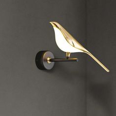 a white bird is sitting on the wall next to a black light fixture with gold accents