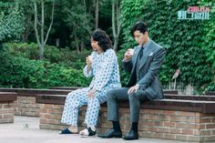 a man and woman sitting on a brick bench eating food together in front of some trees