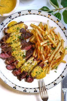 a plate with steak, fries and cheese on it next to some dipping sauces