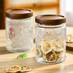 two glass jars filled with dried fruit sitting on top of a wooden table next to a cutting board