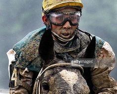 a man riding on the back of a brown horse wearing goggles and a yellow hat