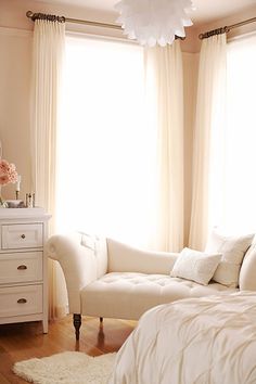 a white couch sitting in front of a window next to a dresser and bed with pillows on top of it