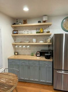 a kitchen with gray cabinets and wood floors, an old clock on the wall above the refrigerator