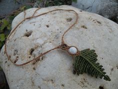 a green leaf and white bead necklace on a rock