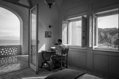 a man sitting at a desk in front of two windows looking out onto the ocean