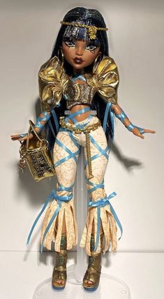 a doll is dressed in gold and blue clothing with her hands out to the side