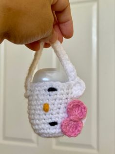 a hand holding a crocheted hello kitty cup holder with a pink flower on it