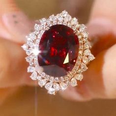 a close up of a person holding a ring with a large red stone