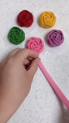 a person holding a pink toothbrush in front of four different colored rolled doughs