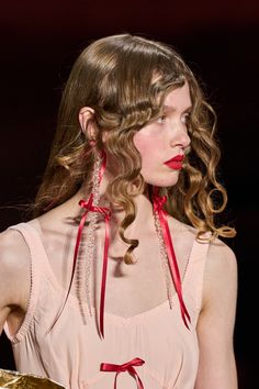 a woman with curly hair and red lipstick on the catwalk at a fashion show