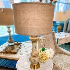 a lamp sitting on top of a white table next to a chair with flowers in it