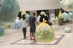 two people standing in front of bags filled with plastic waste sitting on the floor next to each other