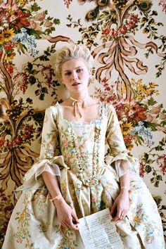 a woman sitting on top of a chair in front of a wall covered in flowers