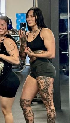two women with tattoos standing next to each other in front of a gym equipment rack