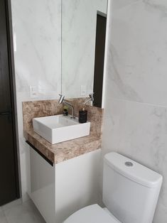 a white toilet sitting next to a bathroom sink under a mirror on top of a counter