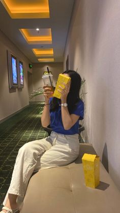 a woman sitting on top of a couch next to a wall holding a yellow box