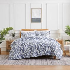 a bed with blue and white comforter in a room next to two potted plants