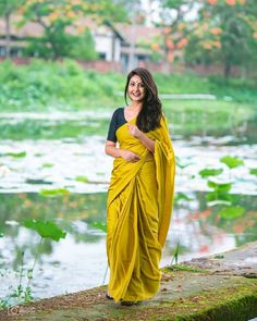 a woman in a yellow sari standing on a rock near water and lily pads