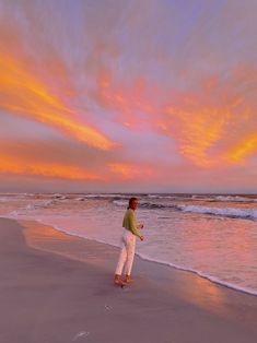 a man standing on top of a beach next to the ocean under a colorful sky