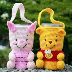 two crocheted winnie the pooh and piglet mug cozies sitting on rocks