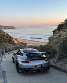 a silver sports car parked on the side of a road next to the ocean at sunset