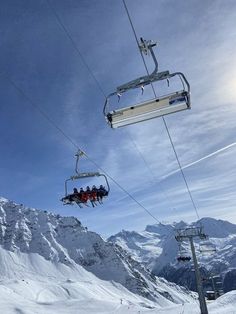 two ski lifts with people riding down the side of it and snow covered mountains in the background