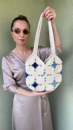 a woman holding up a white purse with blue flowers on the front and sides, in front of a green wall