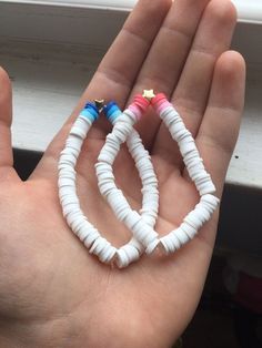 two small white and blue bracelets are held in someone's hand by a window