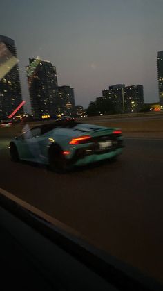 a blue sports car driving down the road in front of some tall buildings at night