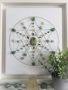 a white framed artwork with green stones and a potted plant