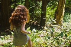 a woman walking in the woods with her back to the camera and looking at trees