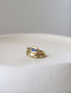 a gold ring sitting on top of a white cake plate with a blue stone in the middle
