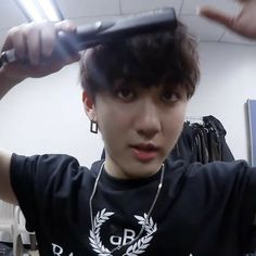 a young man is combing his hair in an office cubicle with two hands