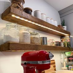 a red mixer sitting on top of a wooden shelf next to jars and other items
