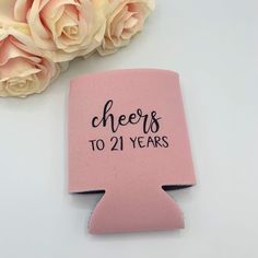 a pink flask with cheers to 21 years written on it next to some flowers