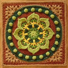 a crocheted square with green and yellow flowers in the center on a wooden surface