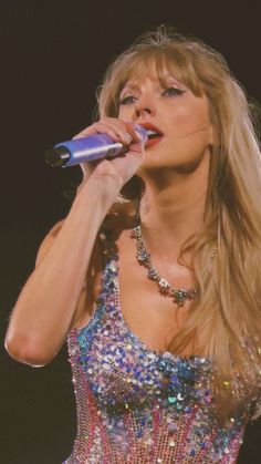 a woman with long blonde hair wearing a dress and holding a microphone in her hand