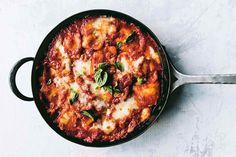 a skillet filled with pasta and sauce on top of a white table next to a spoon