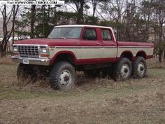 an old red and white truck parked in a field with trees in the back ground