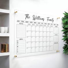 a wall calendar hanging on the wall next to a potted plant and mugs