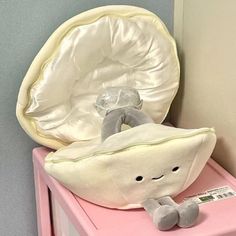 a stuffed animal sitting on top of a pink table next to a white and gray pillow