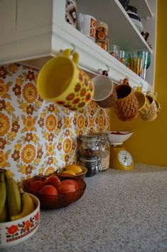 the kitchen counter is full of fruit and coffee mugs hanging from hooks on the wall