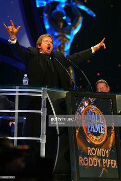 a man in a tuxedo standing at a podium with his hands up