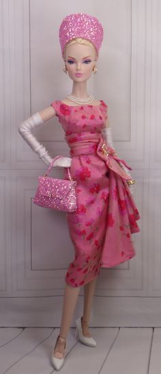 a barbie doll wearing a pink dress and hat with purses on her hand, in front of a white wall