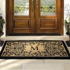 a door mat with the letter m on it and potted plants in front of it