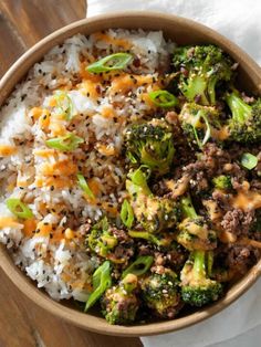 a bowl filled with rice, meat and broccoli on top of a wooden table