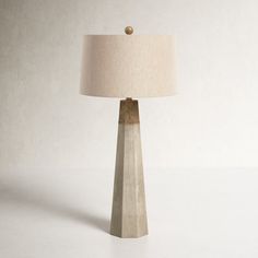 a table lamp with a beige shade on it and a white wall in the background