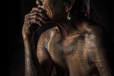 an old woman with tattoos on her chest and hands to her face, in the dark