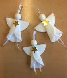 three white angel ornaments with gold stars hanging from strings on a wooden table, ready to be made into christmas ornament decorations