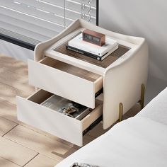 a nightstand with two drawers and a book on the bottom shelf next to a bed